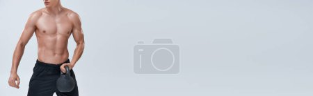 Foto de Recortado vista de hombre atlético en pantalones deportivos posando en topless mientras se ejercita con kettlebell, bandera - Imagen libre de derechos