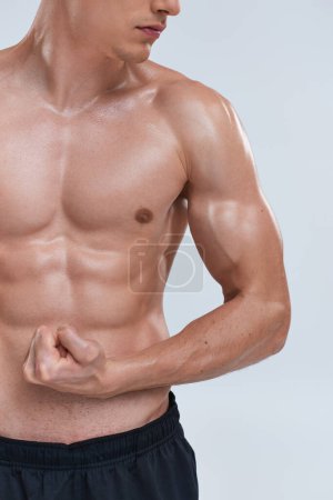 Foto de Recortado vista de hombre atlético posando en topless sobre fondo gris y jugando sus músculos en la cámara - Imagen libre de derechos