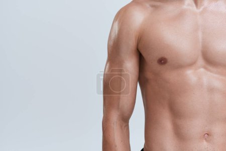 Foto de Recortado vista de hombre atlético posando en topless sobre fondo gris y jugando sus músculos en la cámara - Imagen libre de derechos