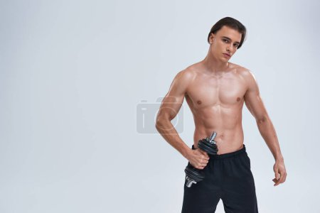 atractivo atlético hombre posando en topless ejercicio activamente con la mancuerna y mirando a la cámara