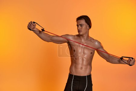 attractive young sporty man in black shorts posing topless and exercising with fitness expander