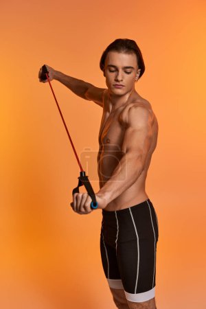 attractive young sporty man in black shorts posing topless and exercising with fitness expander