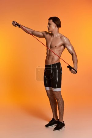 attraktiver junger, sportlicher Mann in schwarzen Shorts posiert oben ohne und trainiert mit Fitness-Expander