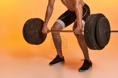 Photo for Cropped view of young sporty man posing shirtless exercising with barbell on vibrant background - Royalty Free Image