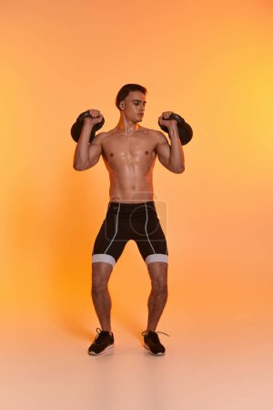 schöner sportlicher Mann ohne Hemd, der mit Kettlebells trainiert und vor orangefarbenem Hintergrund wegschaut
