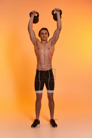 Photo for Appealing sporty shirtless man exercising with kettlebells and looking at camera on vivid backdrop - Royalty Free Image