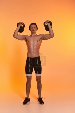 attraktiver sportlicher Mann ohne Hemd, der mit Kettlebells trainiert und vor lebendiger Kulisse in die Kamera blickt