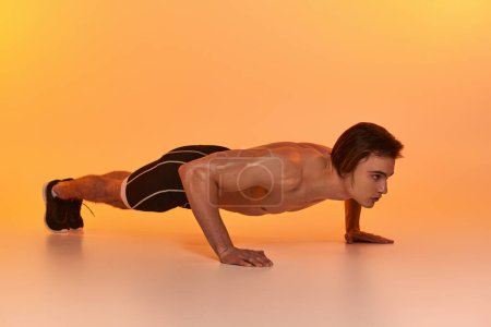 good looking shirtless man in black shorts exercising actively and looking away on orange backdrop