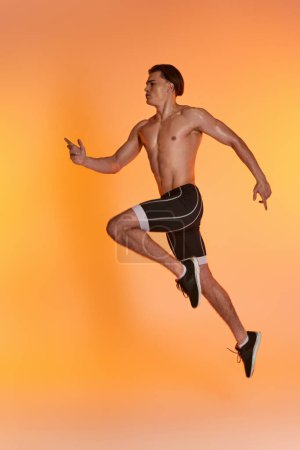 appealing shirtless man in black shorts exercising actively and looking away on orange backdrop