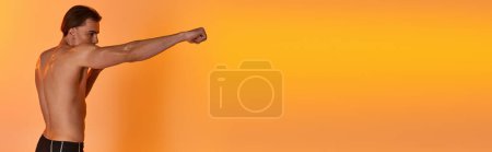 Photo for Alluring shirtless sexy man in black shorts boxing actively on vibrant orange background, banner - Royalty Free Image