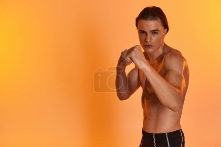 Foto de Atractivo joven musculoso hombre en pantalones cortos posando en topless y boxeo activamente y mirando a la cámara - Imagen libre de derechos