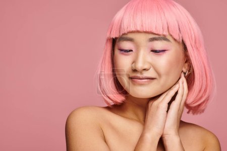 pretty asian woman with pink hair and makeup looking to down with hands on vibrant background