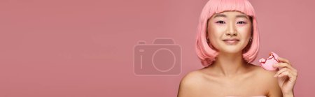 Foto de Banner de mujer asiática con pelo rosa y maquillaje posando con mordida de macarrón sobre fondo vibrante - Imagen libre de derechos