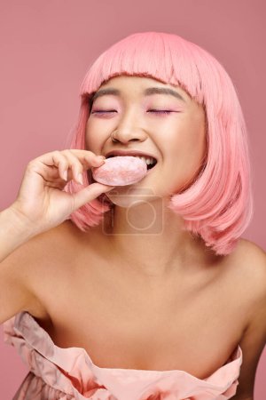 attraktive asiatische junge Frau mit rosa Haaren und geschlossenen Augen, die Mochi vor lebendigem Hintergrund isst