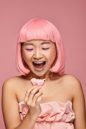 schöne asiatische junge Frau mit rosa Haaren überrascht von mochi vor lebendigem Hintergrund