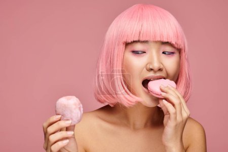 schöne asiatische junge Frau mit rosa Haaren essen Süßigkeiten vor lebendigem Hintergrund