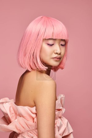 séduisante asiatique jeune femme avec des cheveux roses et haut posant et regardant vers le bas en arrière-plan vibrant