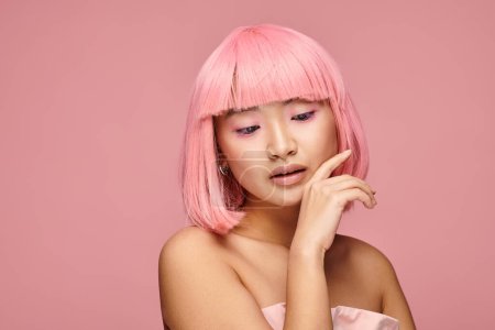 alluring asian young woman with pink hair touching to chin and looking to down in vibrant background