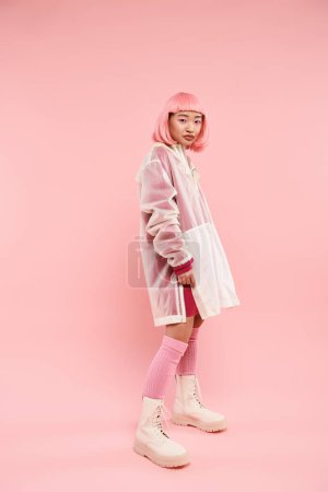 Charmante asiatische junge Frau mit rosa Haaren in stilvollem Outfit posiert seitlich auf lebendigem Hintergrund