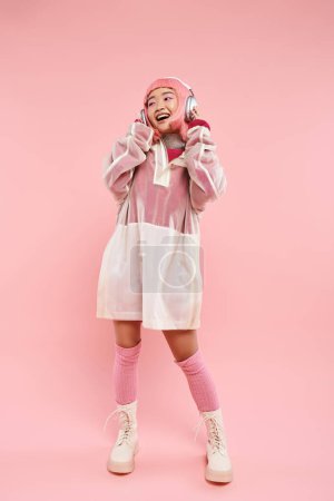 Téléchargez les photos : Heureux asiatique jeune femme avec rose cheveux écoute musique avec casque sur fond vibrant - en image libre de droit