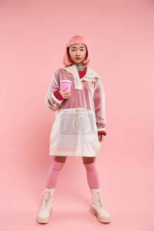 charming asian young woman in pink stylish outfit posing with cup of coffee on vibrant background