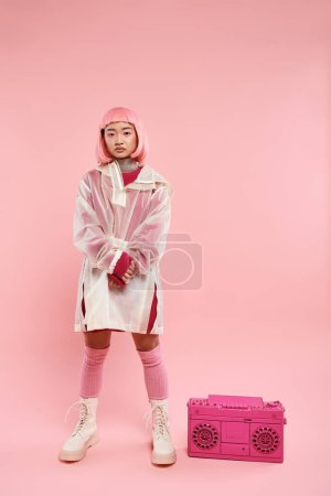 confiado asiático joven mujer con rosa pelo posando con boombox en vibrante fondo