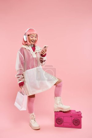hermosa mujer asiática en auriculares mensajes de texto en el teléfono inteligente y la celebración con paquetes de compras