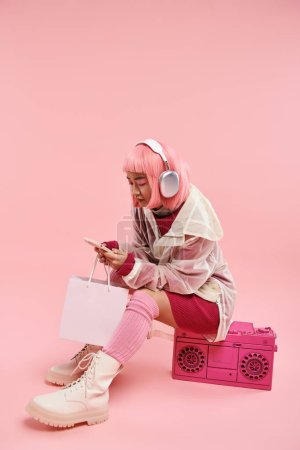 attractive asian young in headphones texting in smartphone and sittings on boombox