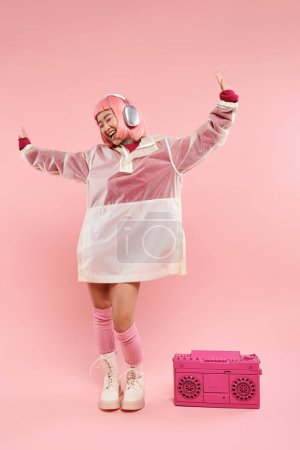 feliz asiático joven mujer con rosa pelo en auriculares bailando con música en vibrante fondo