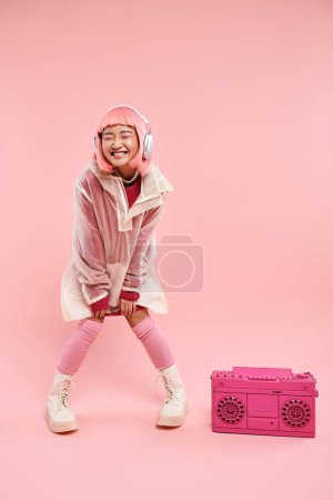 beautiful asian woman with pink hair in headphones posing with boombox in vibrant background