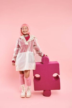 niedliche asiatische junge Mädchen mit rosa Haaren posiert mit großem Puzzle auf lebendigem Hintergrund