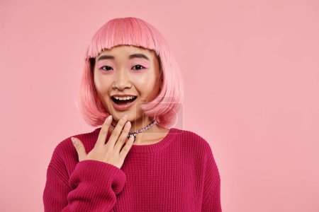 Foto de Feliz chica asiática en suéter vibrante con collar de perlas expresando admiración sobre fondo rosa - Imagen libre de derechos