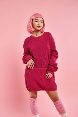encantadora joven con el pelo rosa y maquillaje en traje de suéter grande contra fondo vibrante