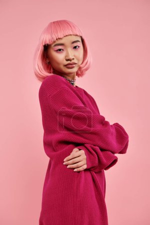 gentle asian young woman with pink hair in sweater outfit hugging herself and looking to camera