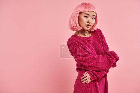 playful and attractive asian woman in her 20s posing with hands against pink background