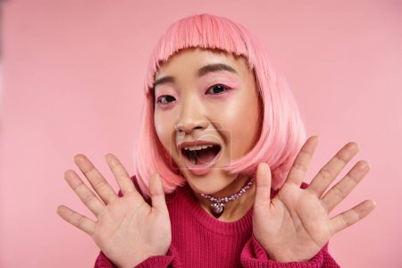 süßes asiatisches Mädchen in den 20er Jahren mit rosa Haaren drückt Bewunderung mit den Händen auf lebendigem Hintergrund aus