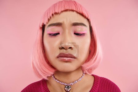 close up of young woman with nose piercing looking to down with disgust on pink background