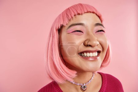close up of asian young woman with nose piercing happy laughing on pink background