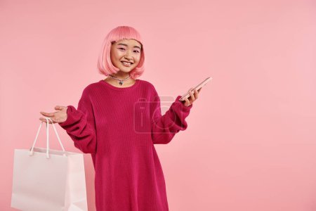 Téléchargez les photos : Attrayant asiatique fille avec rose cheveux et maquillage se livrer à des achats en ligne sur fond vibrant - en image libre de droit