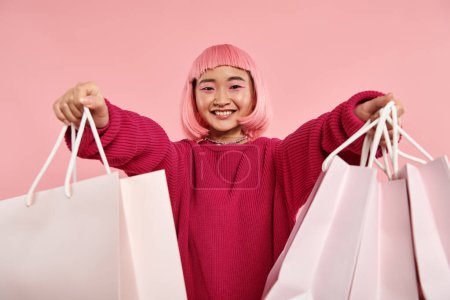 beautiful asian young girl smiling broadly and holding out to shopping bags on pink background