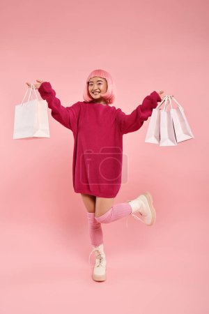 süße asiatische Frau in ihren Zwanzigern posiert mit erhobenem Bein und hält Einkaufstüten auf rosa Hintergrund