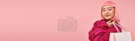 Horizontale Ansicht einer attraktiven asiatischen Frau in den 20er Jahren, die mit Päckchen vor rosa Hintergrund posiert