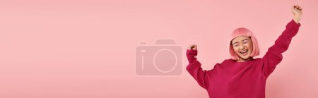 horizontale Aufnahme einer charmanten asiatischen Frau in den 20er Jahren mit rosa Haaren sehr glücklich auf lebendigem Hintergrund
