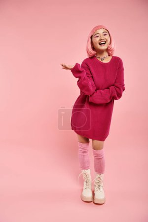 fröhliche asiatische junge Frau mit pinkfarbenen Haaren im Pullover-Outfit lacht vor lebendigem Hintergrund