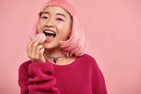 Porträt einer fröhlichen asiatischen Frau mit rosa Haaren, die Mochi mit Bewunderung vor lebendigem Hintergrund isst
