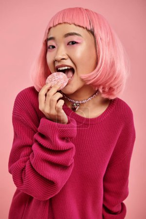 hermosa asiática joven chica con rosa pelo y maquillaje comer mochi en vibrante fondo