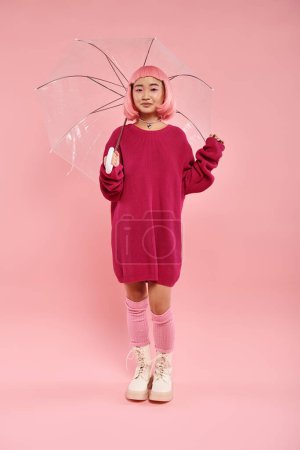 Téléchargez les photos : Attrayant jeune femme en tenue élégante debout sous le parapluie sur fond rose - en image libre de droit