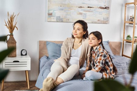 Téléchargez les photos : Une mère et sa fille assises sur un lit confortable, profitant de moments de qualité ensemble à la maison. - en image libre de droit
