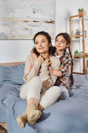 Une mère et sa fille assises ensemble sur un lit, partageant un moment spécial et aimant à la maison.