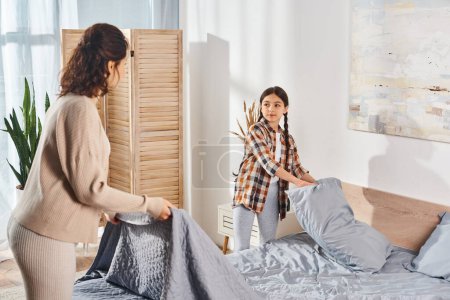 A woman and her daughter standing next to a bed in a cozy bedroom, sharing a tender moment together.